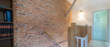 A staircase with a brick wall, a wooden railing, and a bookshelf with books.