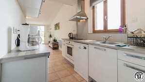A modern kitchen with white cabinets, a stainless steel range hood, a built-in oven, a dishwasher, and a window above the sink. - Green Valley - Villaudric (Villaudric)