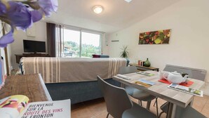A hotel room with a bed, a TV, a dining table with chairs, a painting on the wall, and a sign on the table. - Green Valley - Villaudric (Villaudric)