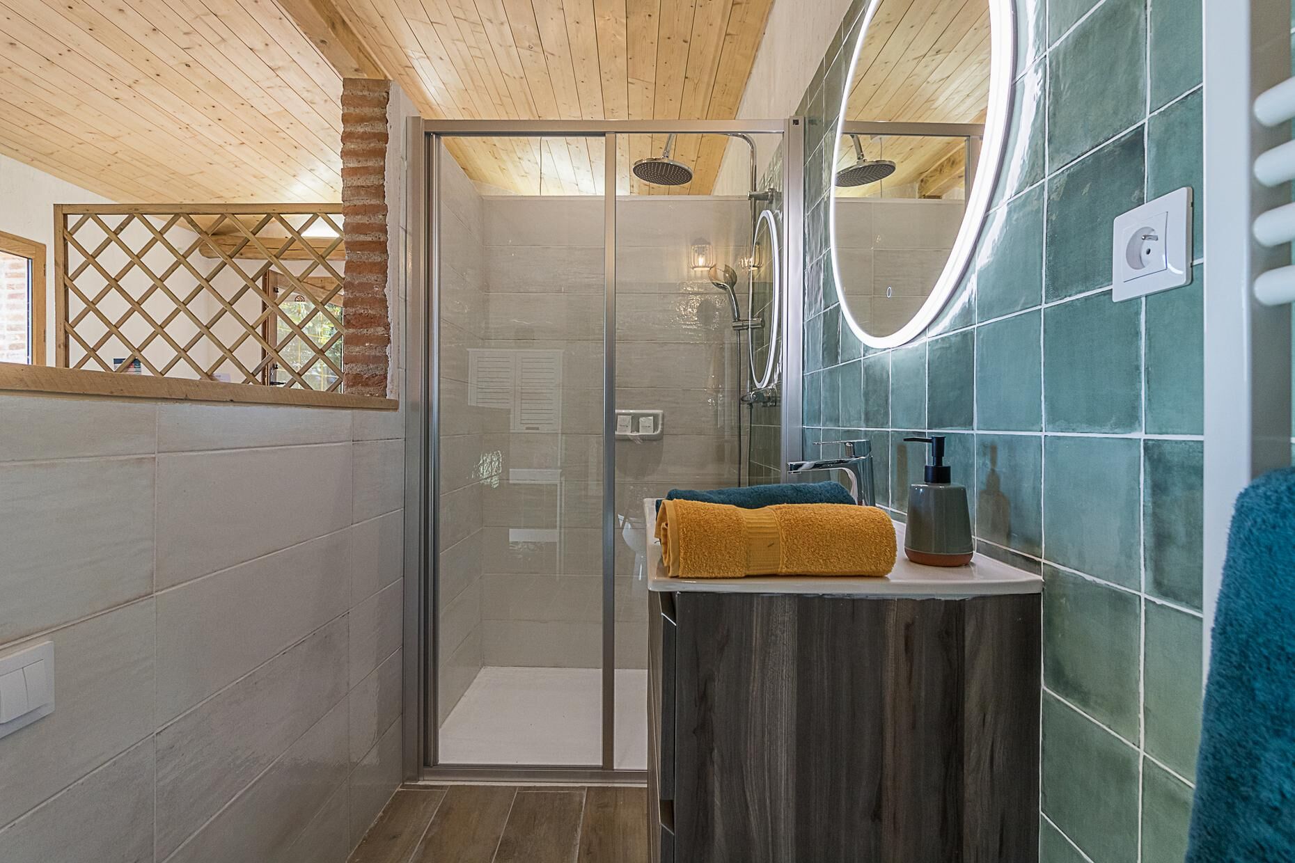 A modern bathroom with a glass shower enclosure, a wooden ceiling, and a tiled wall with a green accent.