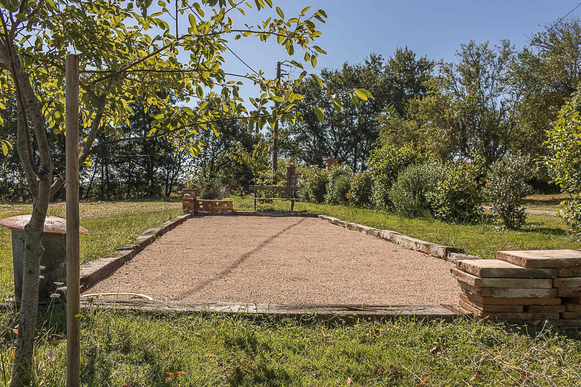 A gravel area with a brick border, surrounded by grass and trees.