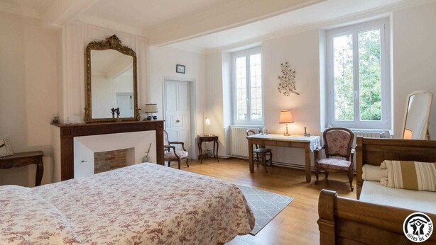 Un dormitorio con una cama grande, un escritorio, dos sillas, una chimenea y ventanas amplias.