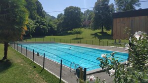 Piscina rectangular con valla, rodeada de césped verde y árboles.