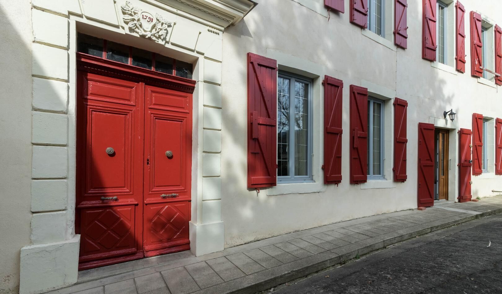A building with a red door and shutters, white walls, and a small window.