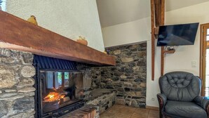 Une cheminée en pierre avec un téléviseur fixé au mur et un fauteuil en cuir.