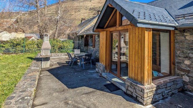 Une maison en pierre avec un porche en bois, une table de patio et des chaises.