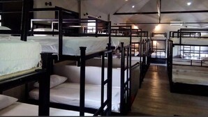 Un dormitorio tipo residencia con literas dispuestas en filas, barandillas de madera y un techo alto con vigas a la vista.