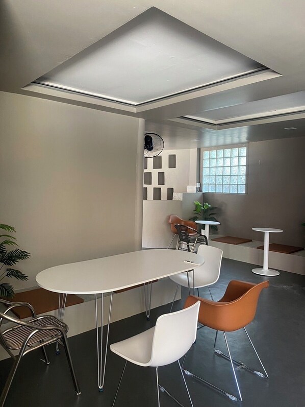 A modern meeting room with a white table, two white chairs, a metal chair, and a small round table. - Hide Hostel (Ko Pha-ngan)