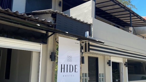 Un edificio moderno de dos pisos con un cartel que dice 'HIDE HOSTEL', publicando información de contacto telefónica y por correo electrónico.