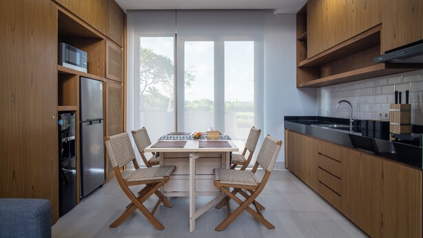 Een moderne keuken met houten kastjes, een ingebouwde magnetron, een koelkast en een eethoek met een tafel en stoelen.