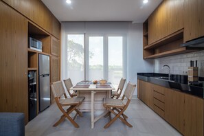 A modern kitchen with wooden cabinets, a built-in microwave, a refrigerator, and a dining area with a table and chairs. - Nusa Djiwa (Tabanan)