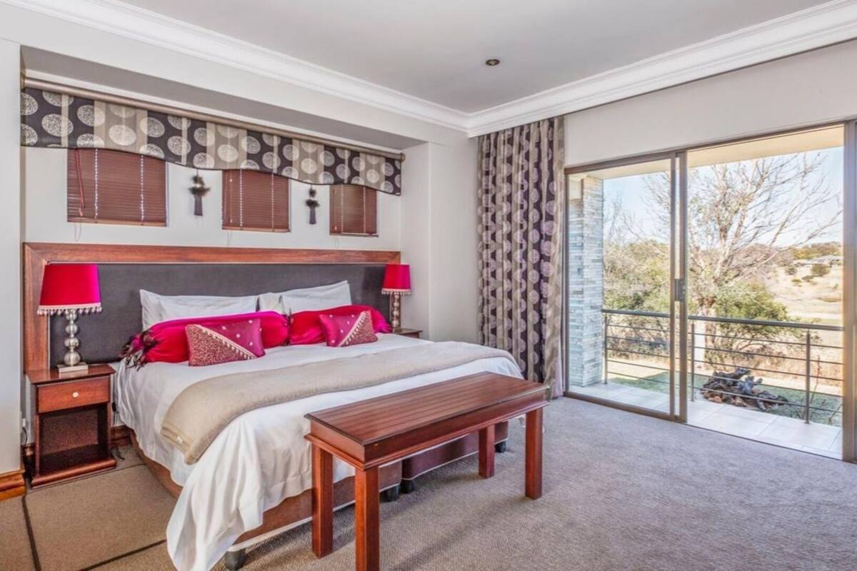 Ein geräumiges Schlafzimmer mit einem großen Bett, zwei Nachttischen, einer hölzernen Bank und einem Balkon mit Blick ins Freie.