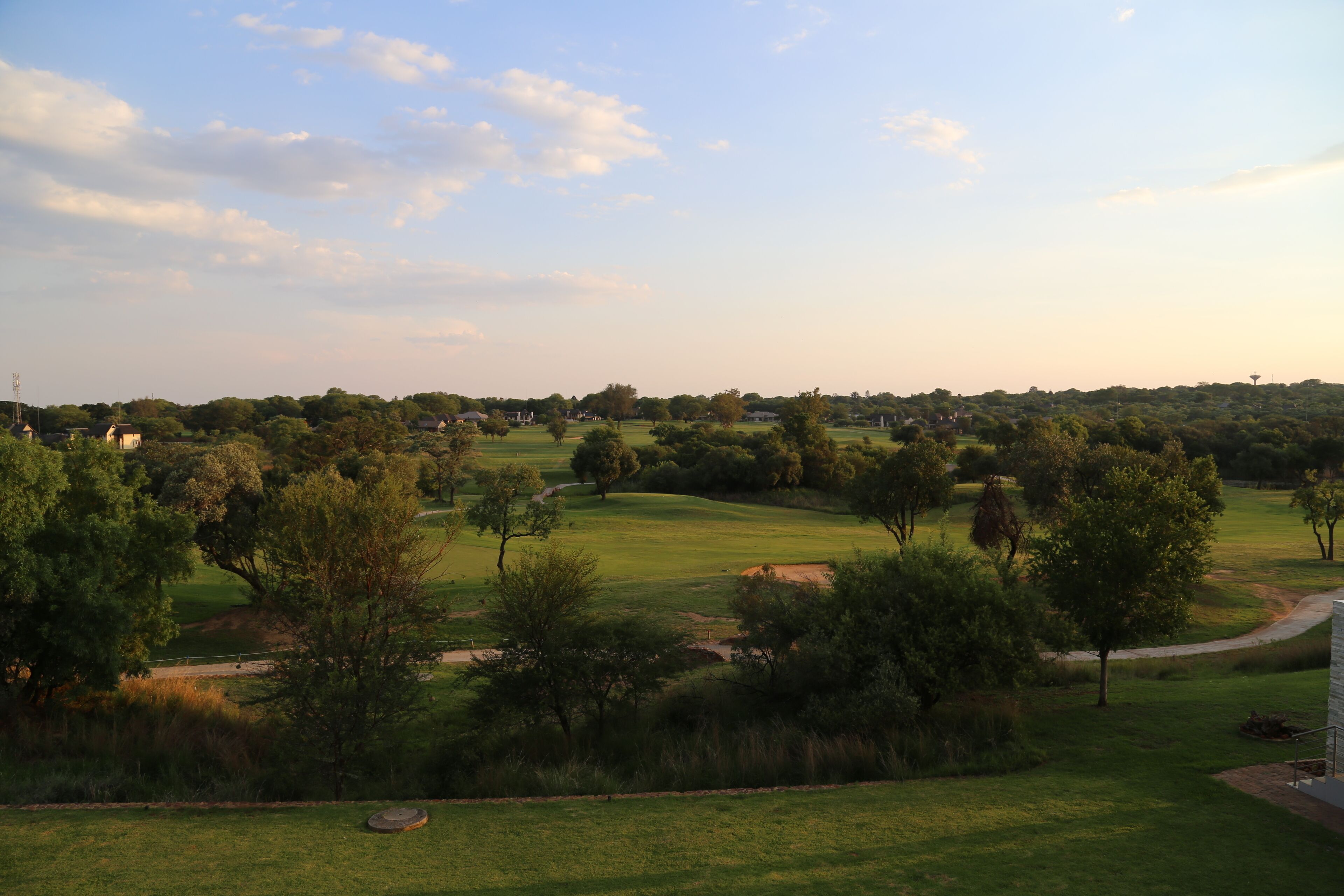 A golf course with a clear path, trees, and a distant building.