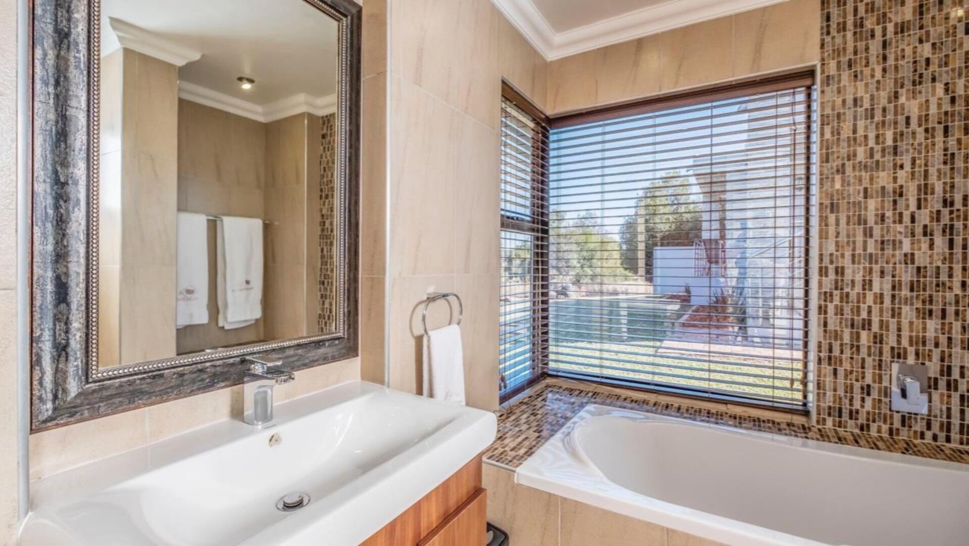 A bathroom with a large mirror, a bathtub, and a window with blinds.