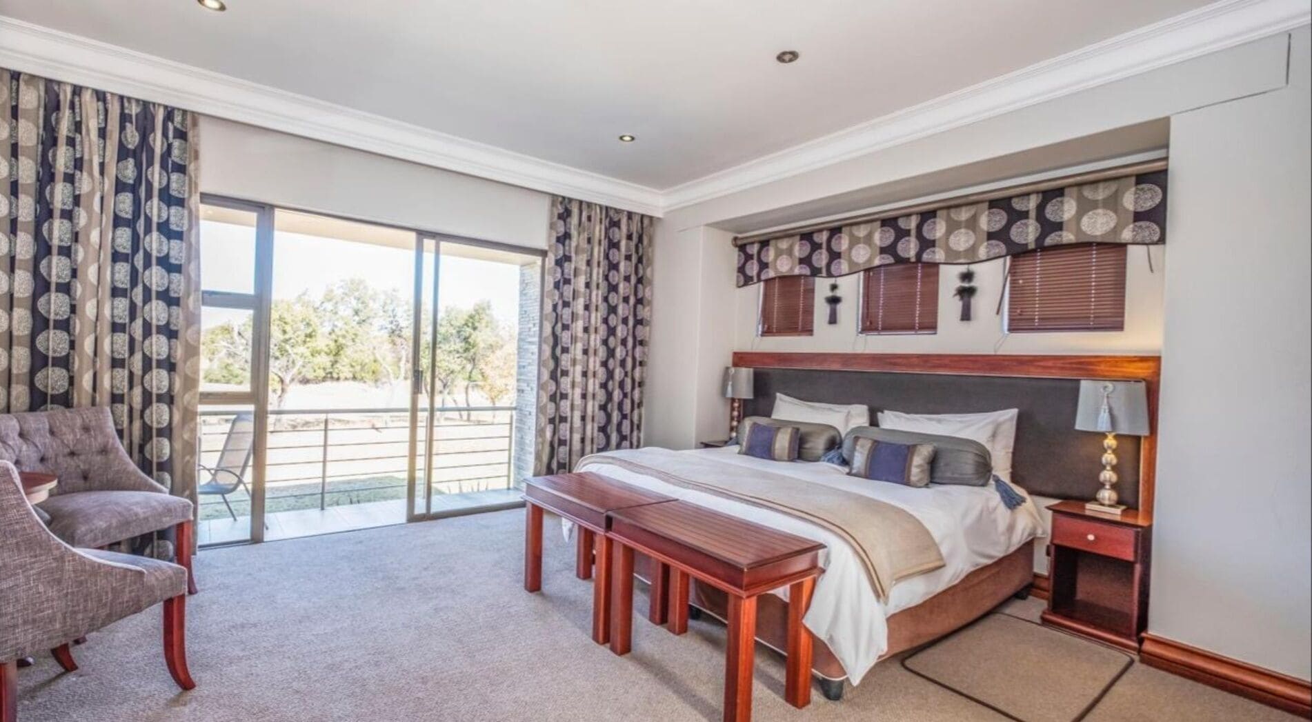 A bedroom with a bed, a chair, a bench, and a view of the outdoors.