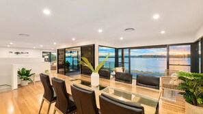 A modern dining area with a glass table, black chairs, and a view of a lake.