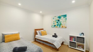 A bedroom with two beds, a bookshelf, and a painting.