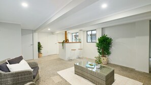 A spacious living area with a wicker sofa, a glass coffee table, and a bar area with stools.
