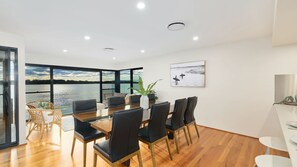 A modern dining area with a view of a lake, a large table with chairs, and a potted plant.