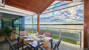 Comedor con una mesa lista para cuatro, con vistas a un cuerpo de agua y un cielo nublado.