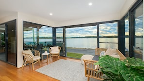 Interior moderno com grandes janelas, área de estar com móveis de vime e vista para um lago.