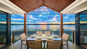 Un comedor con una mesa preparada para cuatro, con vista a un cuerpo de agua y una vista del atardecer.