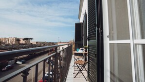A balcony with a table and chairs, overlooking a street with cars and buildings.