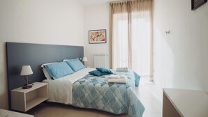 A modern bedroom with a large bed, a nightstand, a bedside table, and a window with curtains.