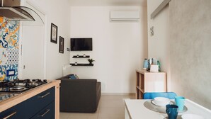 A modern kitchen with a stove, a dining table with chairs, and a TV mounted on the wall.