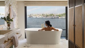 Un baño moderno con una bañera grande, un tocador con espejo y vistas a una masa de agua con barcos.