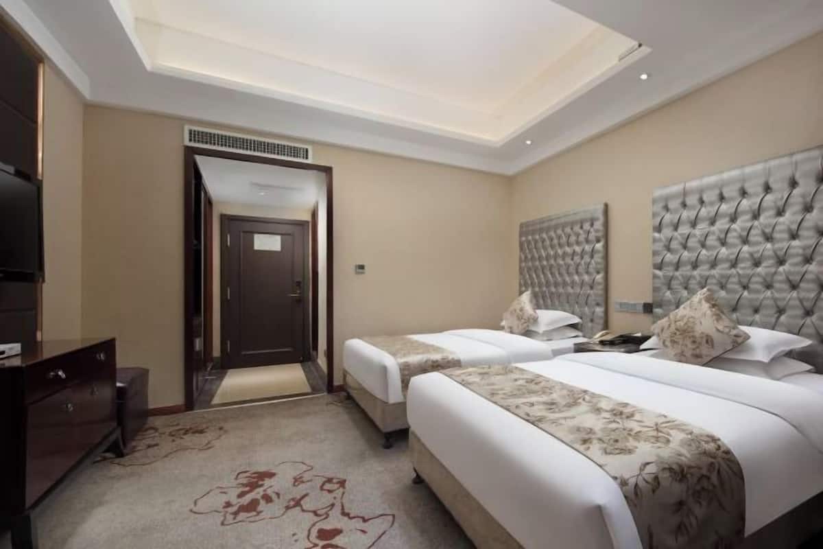 A hotel room with two beds, a large tufted headboard, a flat-screen TV, and a ceiling light fixture.
