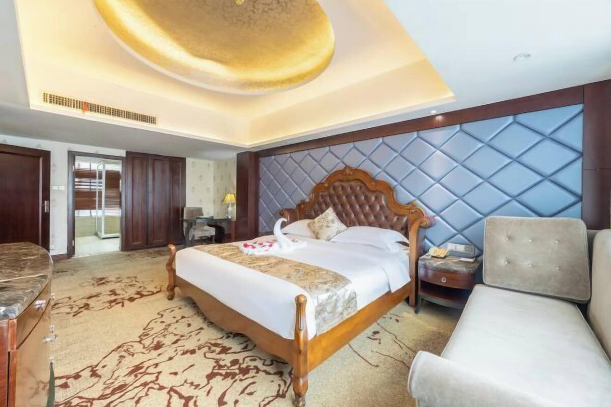A hotel room with a large bed, a sofa, a desk, and a decorative ceiling.