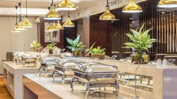 A buffet setup with multiple serving stations, overhead lighting, and decorative plants.