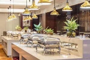 A buffet setup with multiple serving stations, overhead lighting, and decorative plants. - Kaitian Rezen Hotel (Huayuan)