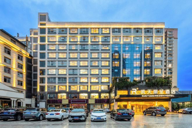 A multi-story hotel with a row of windows on each floor, a parking lot in front, and a sign with Chinese characters.