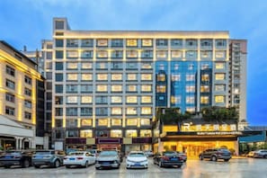 A multi-story hotel with a row of windows on each floor, a parking lot in front, and a sign with Chinese characters. - Kaitian Rezen Hotel (Huayuan)