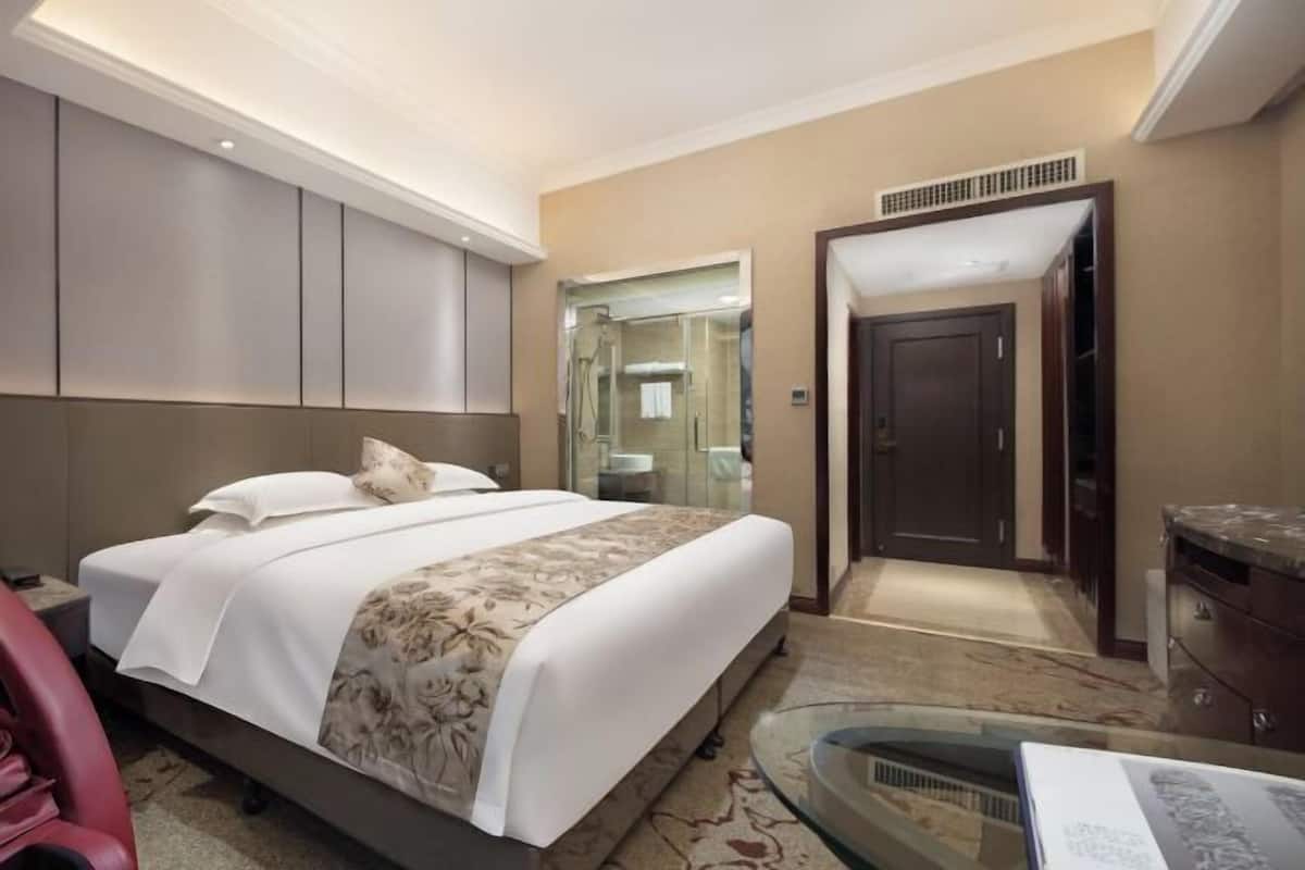 A hotel room with a bed, a glass table, a mirror, a wardrobe, and a door.