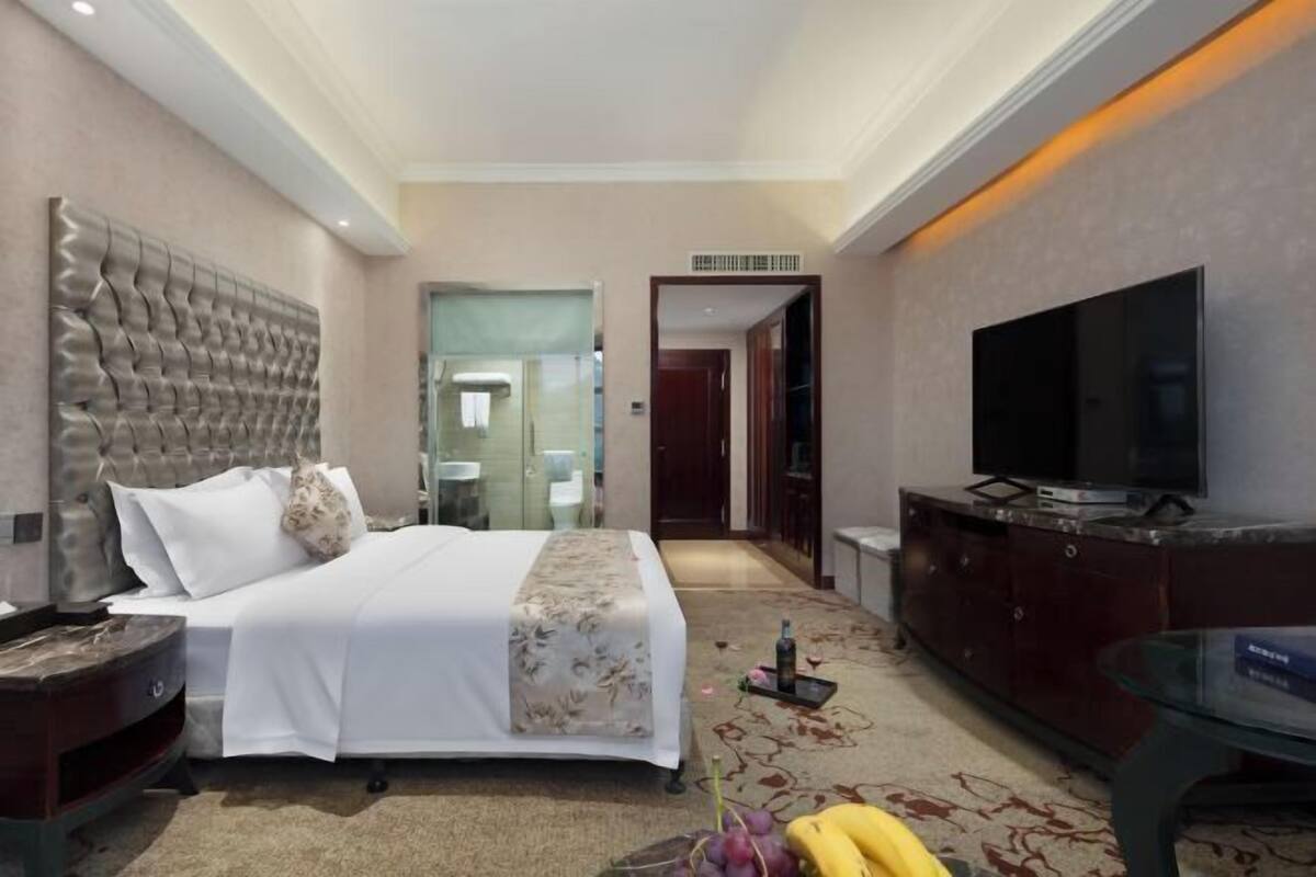 A hotel room with a large bed, a television, a cabinet, and a bathroom visible through an open door.