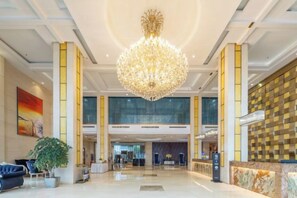 A spacious lobby with a large chandelier, a reception desk, and a modern interior design.