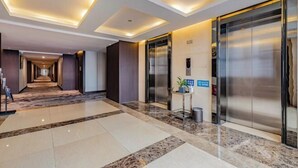 Un hall de hotel con piso de mármol, un largo pasillo y dos ascensores.