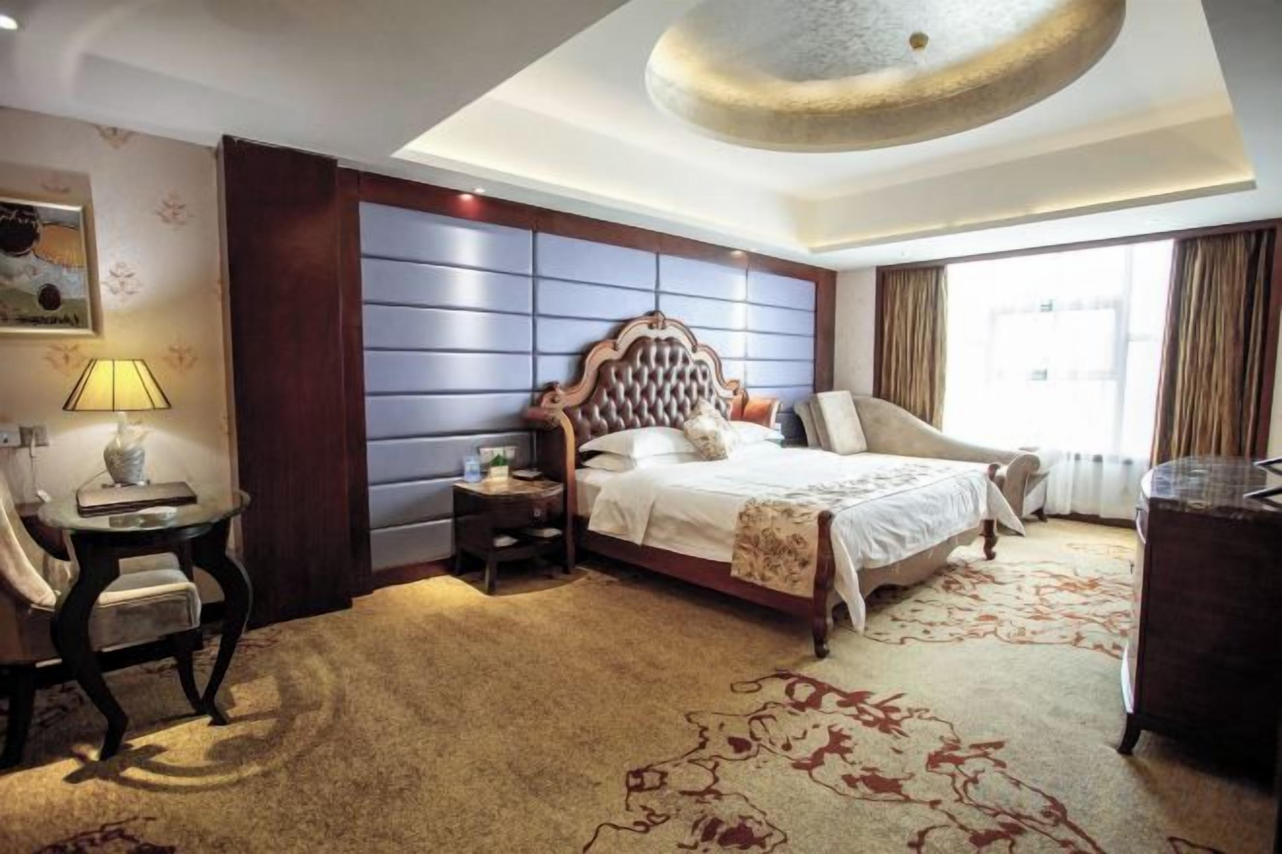 A hotel room with a large bed, a desk, a chair, a nightstand, and a window with curtains.