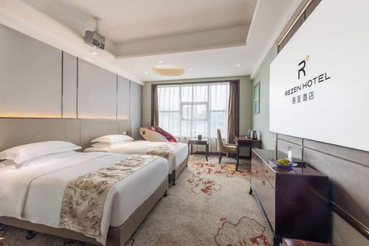 A hotel room with two beds, a desk, a chair, and a large window.