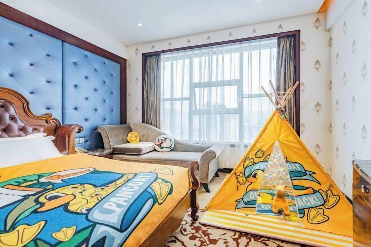 A hotel room with a large bed, a chair, a window with curtains, and a yellow tent.