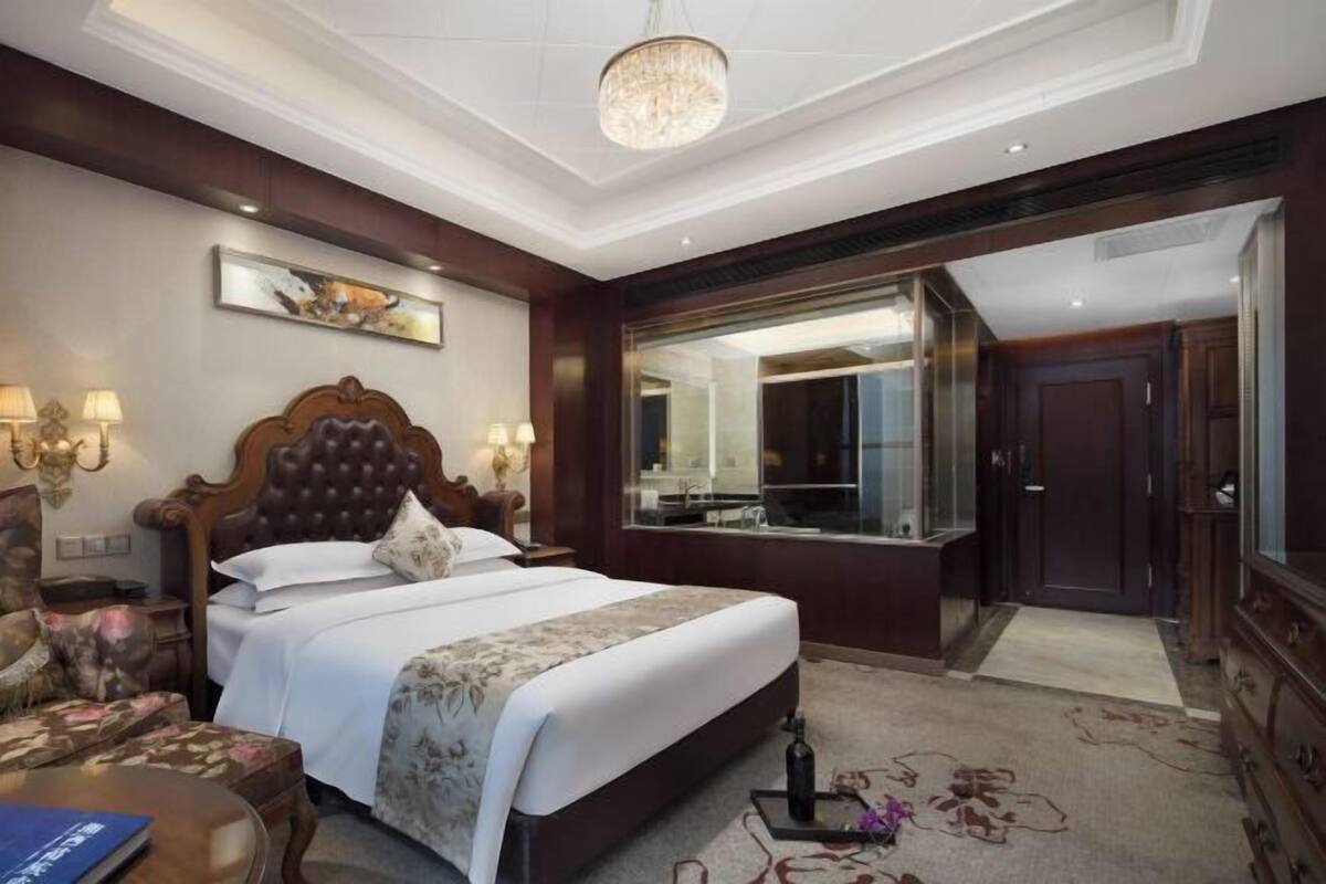 A hotel room with a large bed, a mirror, a wardrobe, and a chandelier.