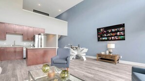 A modern living room with a glass coffee table, a blue armchair, and a dining area with a white table and chairs.