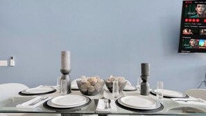 A modern dining room with a glass table set for two, surrounded by white chairs.