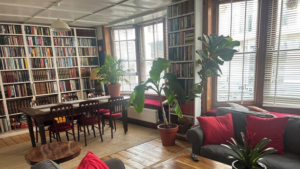 Ein gemütliches Wohnzimmer mit Bücherregal, Esstisch und bequemen Sitzmöglichkeiten.