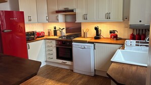 Eine kompakte Küche mit weißen Schränken, einem roten Kühlschrank, einem Gasherd, einem Geschirrspüler und einer Kaffeemaschine.