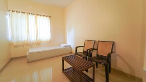 A small, clean room with a bed, two chairs, and a table. - Trattino Resorts (Wai)