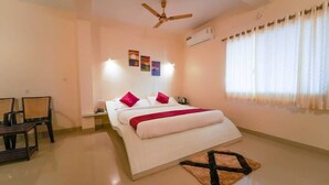 A bedroom with a bed, a ceiling fan, an air conditioner, a window with curtains, and a small table with chairs. - Trattino Resorts (Wai)